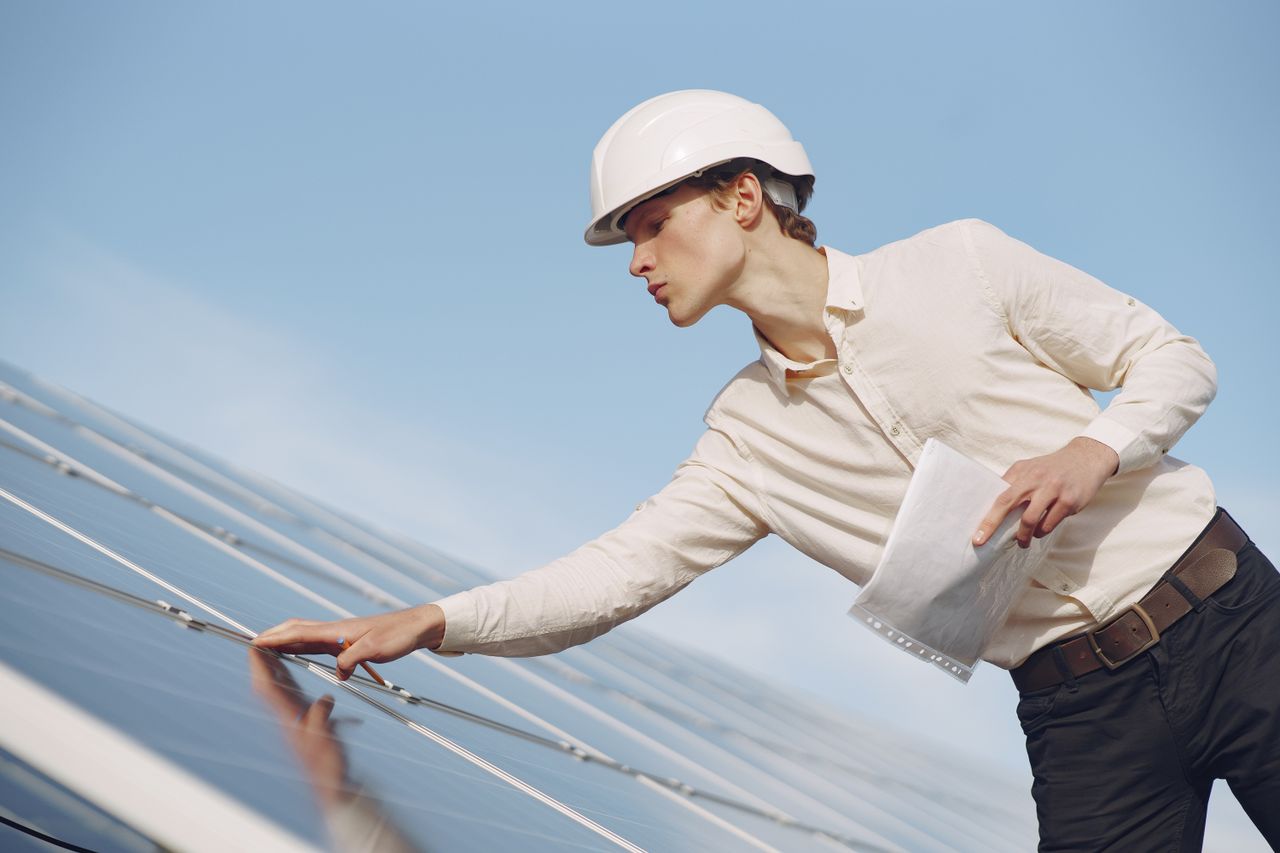 Mastering the First Impression: Your intriguing post title goes here Low angle of young male inspector with documents in formal wear and hardhat standing against solar panels and checking details of construction