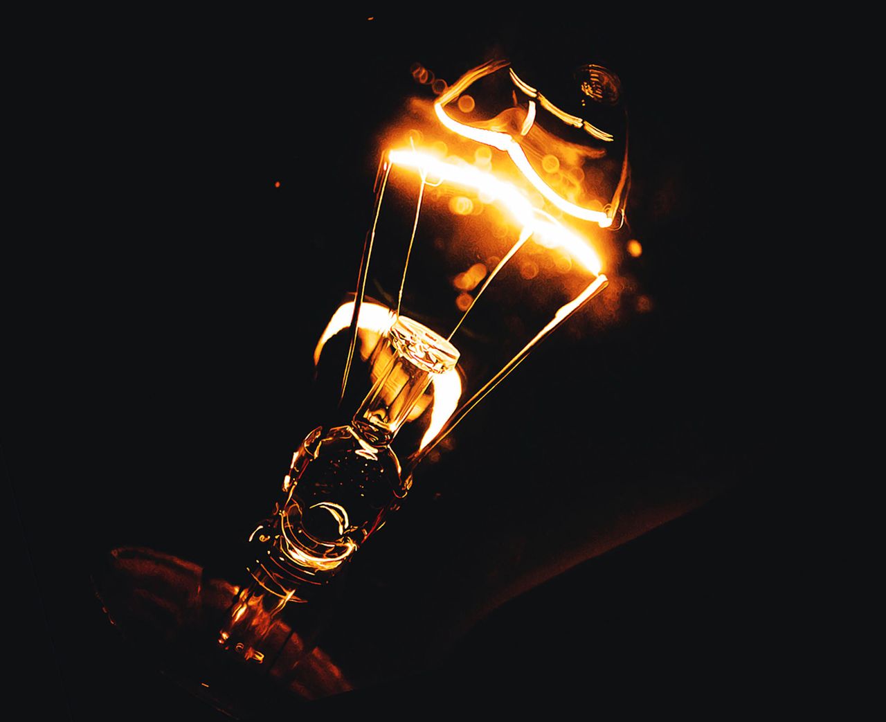Dramatic close-up photo of an illuminated light bulb filament glowing in the dark.